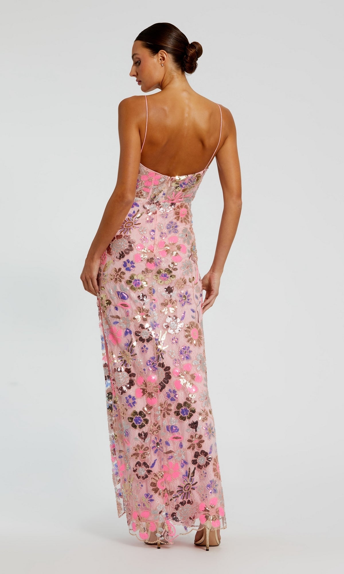 A woman stands facing away from the camera wearing the Long Formal Dress 68718 by Mac Duggal, featuring a pink floral sequin design, v-neckline, thin straps, open back, and a floor-length hem.
